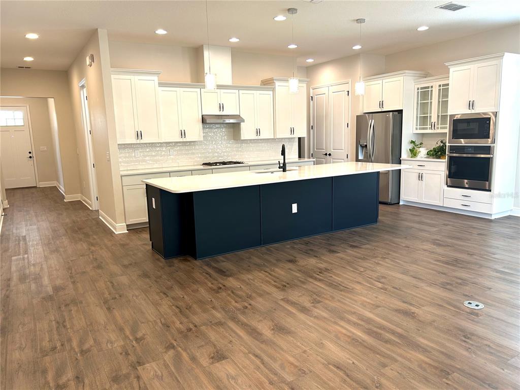 A modern kitchen features a dark blue island, white cabinetry, and light wood-look flooring — 1598 WHITEWOOD COURT, KISSIMMEE, FL