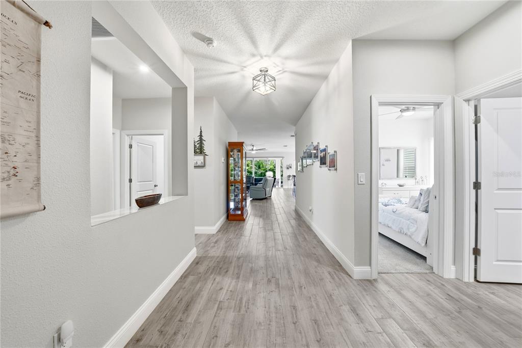 A hallway with light wood-look flooring leads toward a living area with a glass display cabinet — 5521 LIMELIGHT DRIVE, APOLLO BEACH, FL