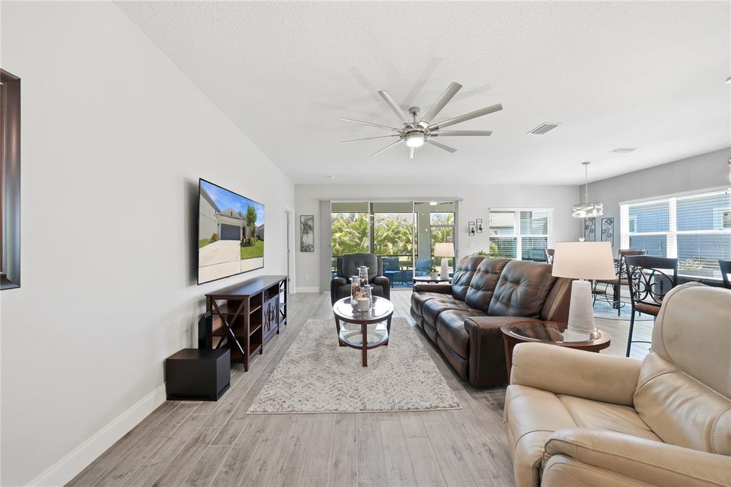A living room features a wall-mounted television, leather sofa, and light wood-look tile flooring — 5521 LIMELIGHT DRIVE, APOLLO BEACH, FL