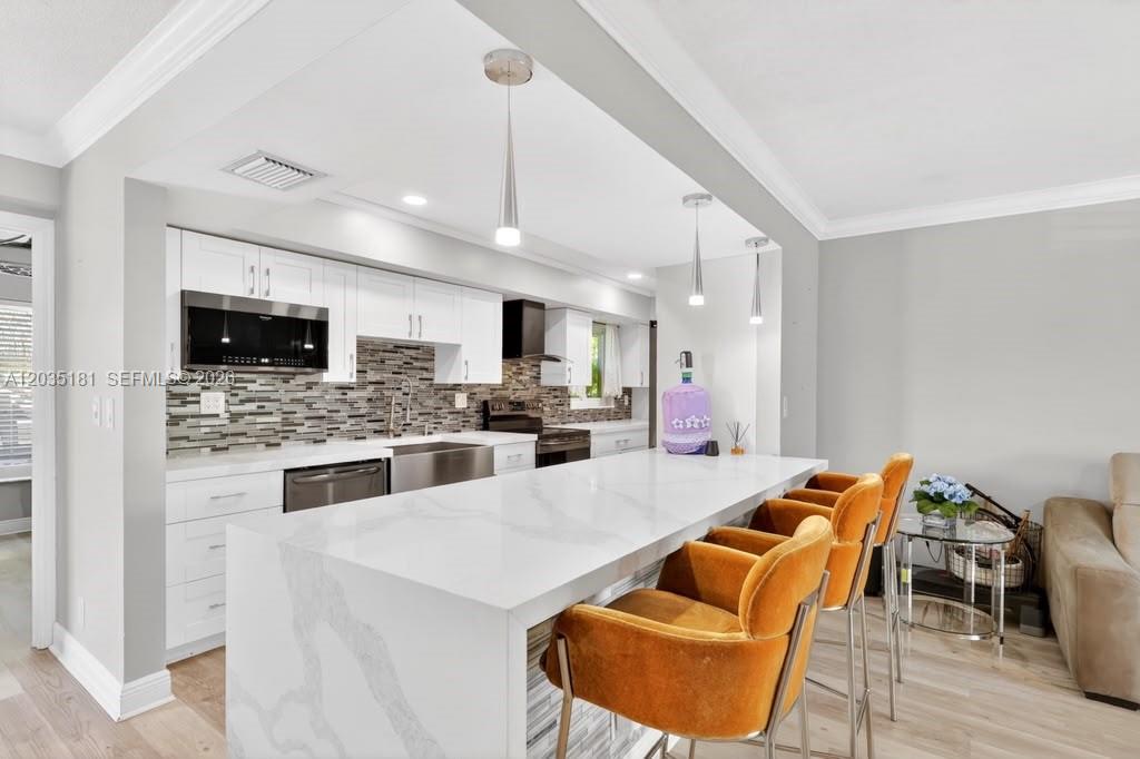 A kitchen features white cabinets, a marble-topped island with orange chairs, and a tiled backsplash — 1000 W River Dr, Margate FL 33063, MARGATE, FL