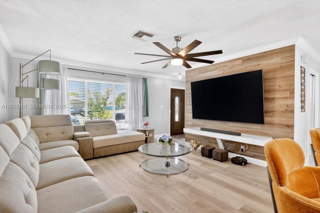 A living room features a large sectional sofa, a wall-mounted television, and wood-look flooring — 1000 W River Dr, Margate FL 33063, MARGATE, FL