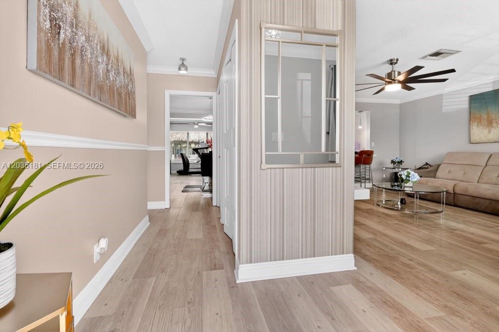 A hallway with light wood flooring leads to a living area and a dining room — 1000 W River Dr, Margate FL 33063, MARGATE, FL