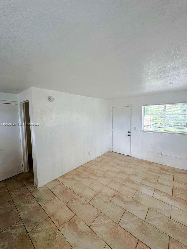 An empty room features white walls, tan tile flooring, a window, and two doors — HOMESTEAD, FL