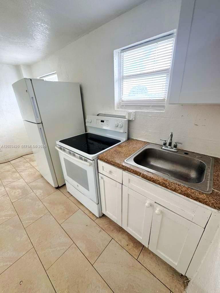 A small kitchen features white cabinets, a stainless steel sink, and a white stove — HOMESTEAD, FL