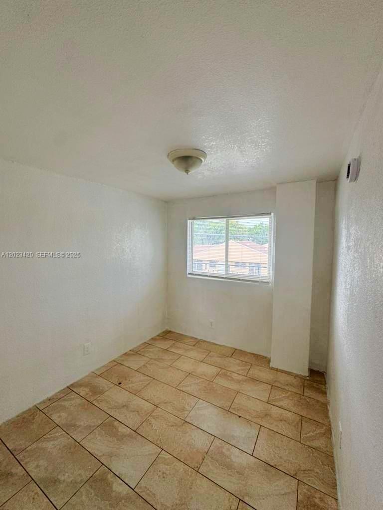 An empty room features white walls, a single window, and light-colored tile flooring — HOMESTEAD, FL