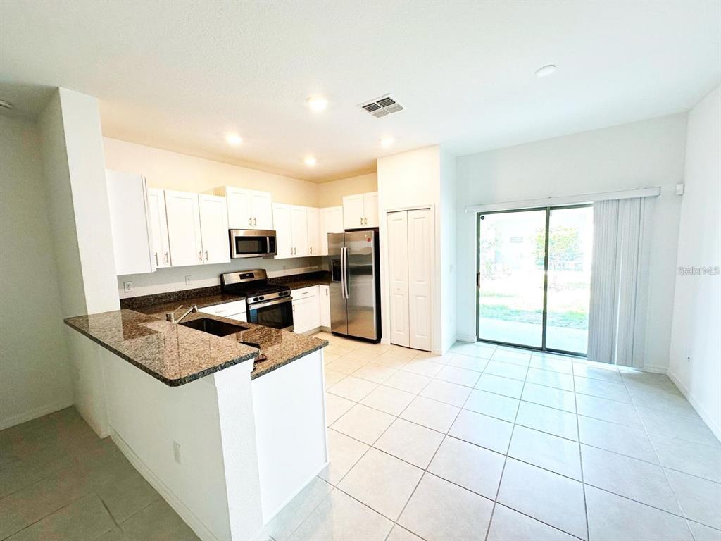 A kitchen with white cabinets, granite countertops, stainless steel appliances, and tile flooring — 8239 CRESCENT OAKS DRIVE, NEW PORT RICHEY, FL