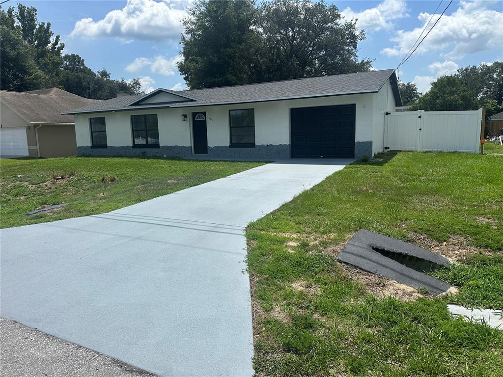 A single-story house with a white facade, black trim, and a freshly painted gray driveway — 113 TEAK LOOP, OCALA, FL