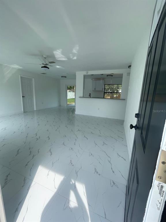 An open-concept living area features white marble-look tile flooring and a kitchen pass-through window — 113 TEAK LOOP, OCALA, FL