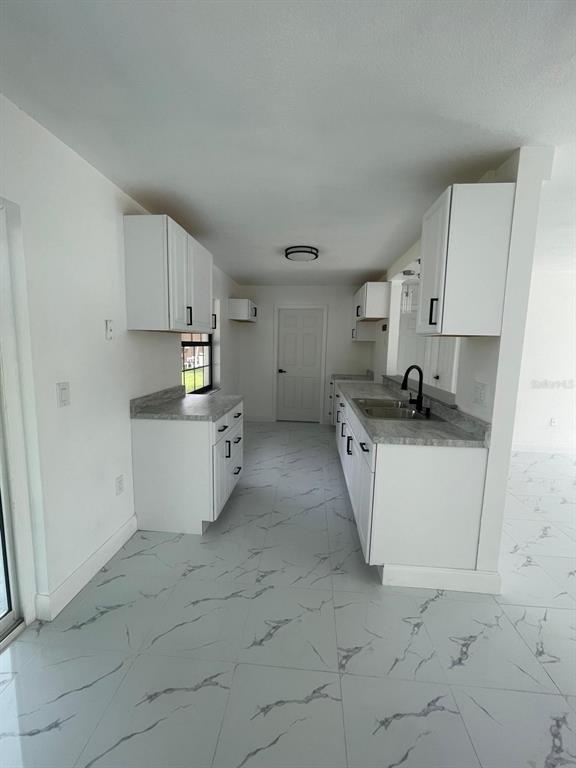 A galley kitchen features white cabinets, gray countertops, and white marble-patterned tile flooring — 113 TEAK LOOP, OCALA, FL