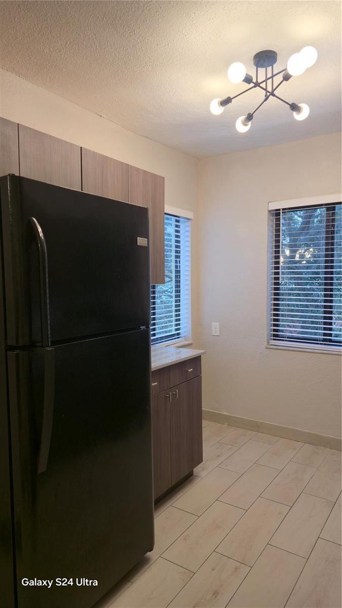 A kitchen features a black refrigerator, wood-tone cabinets, light tile flooring, and a modern light fixture — 360 NW 8th Street # 8, Pompano Beach FL 33060, POMPANO BEACH, FL