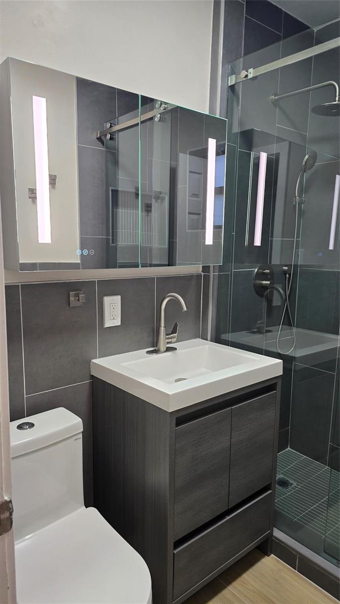 A modern bathroom features a gray vanity, a lighted medicine cabinet, and a glass-enclosed shower — 360 NW 8th Street # 8, Pompano Beach FL 33060, POMPANO BEACH, FL