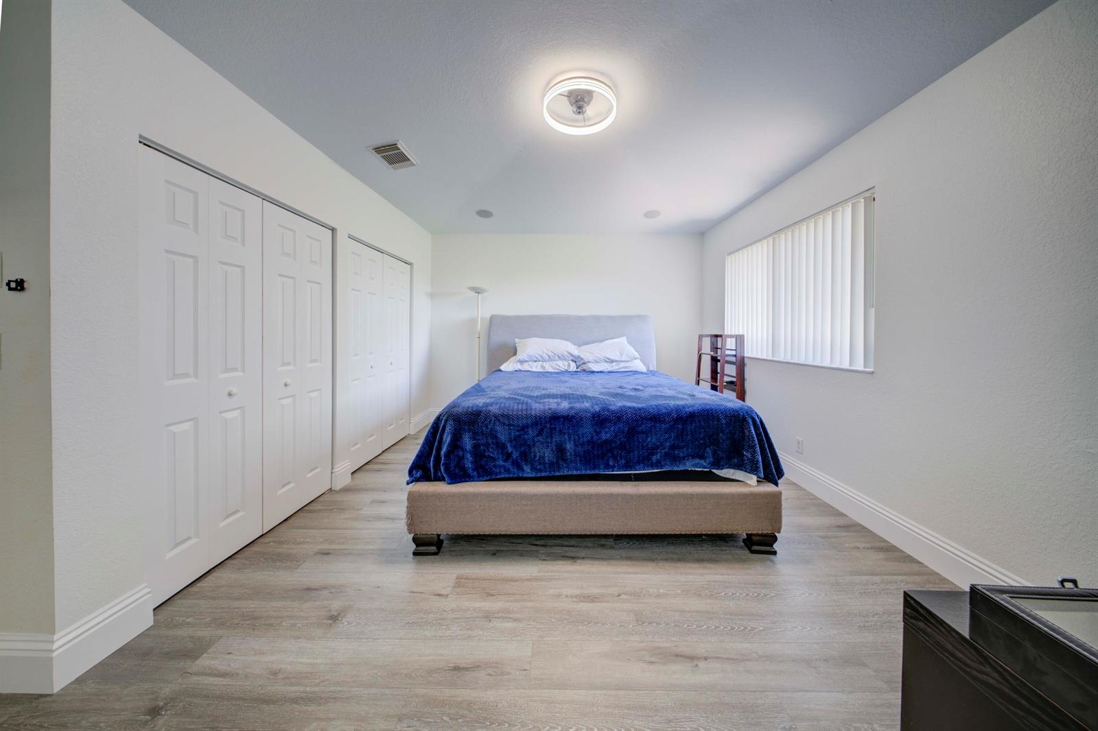 A bedroom features light wood-look flooring, a blue bedspread, white walls, and a ceiling fan — 2364 Center Stone Lane, Riviera Beach FL 33404, RIVIERA BEACH, FL