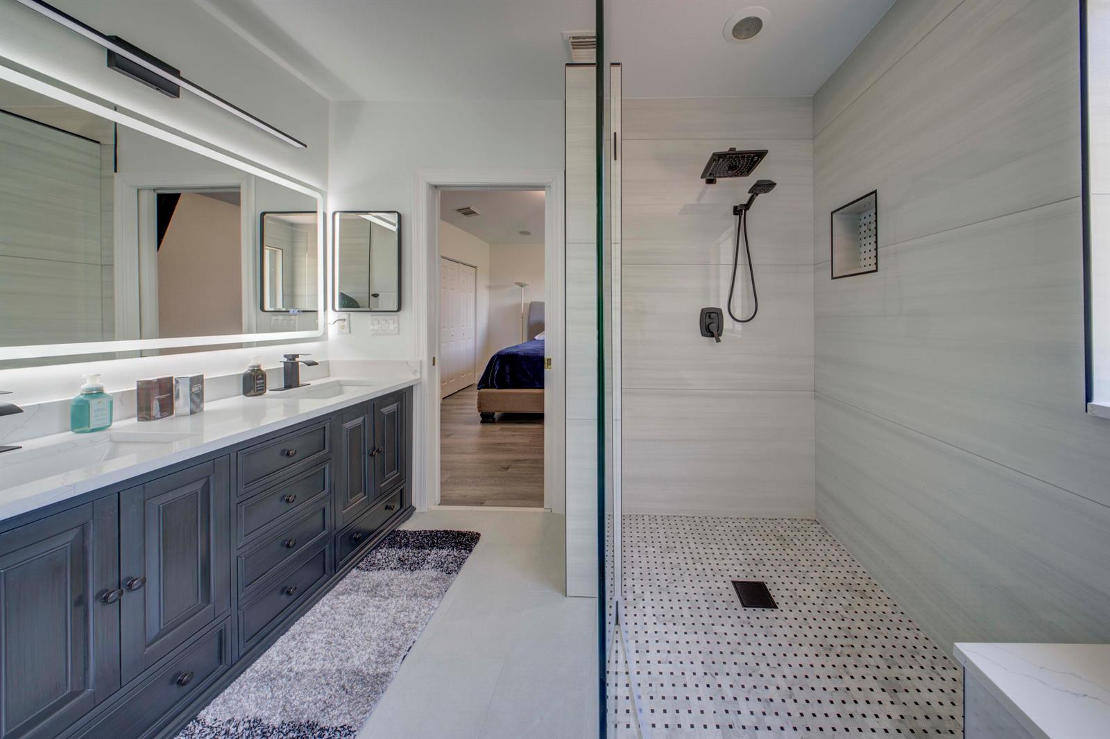 A modern bathroom features a dark gray double vanity, a glass-enclosed shower, and tile flooring — 2364 Center Stone Lane, Riviera Beach FL 33404, RIVIERA BEACH, FL