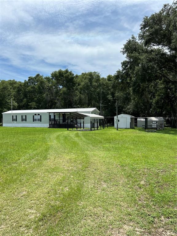A single-story manufactured home with a carport and two storage sheds on a grassy lot — 19449 165 LANE, O'BRIEN, FL