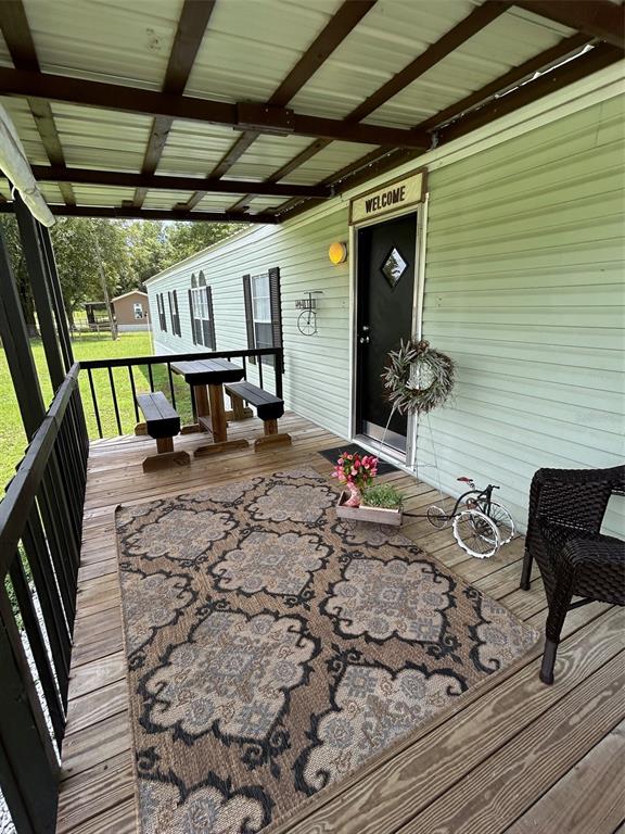A covered wooden porch features a patterned area rug, a small dining set, and a front door — 19449 165 LANE, O'BRIEN, FL