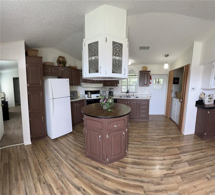 A kitchen features brown cabinets, a white refrigerator, a round island, and wood-look flooring — 19449 165 LANE, O'BRIEN, FL