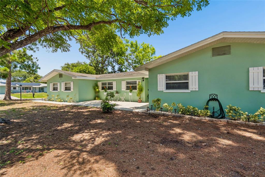 A light green single-story house with white shutters and a paved patio area — 1357 S EVERGREEN AVENUE, CLEARWATER, FL