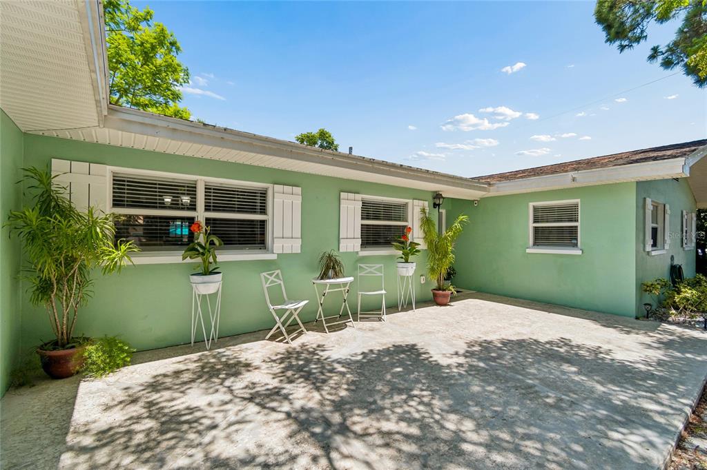 A light green house exterior features a concrete patio with white chairs and potted plants — 1357 S EVERGREEN AVENUE, CLEARWATER, FL