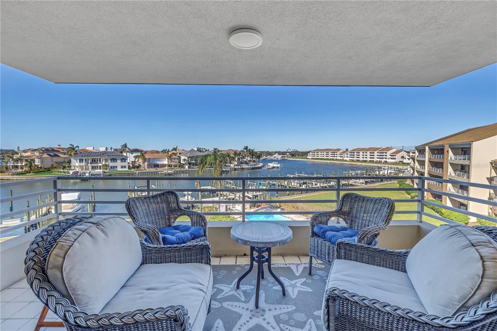 A balcony with wicker furniture overlooks a waterway, boat docks, and residential buildings — 2795 KIPPS COLONY DRIVE S UNIT 305, ST PETERSBURG, FL