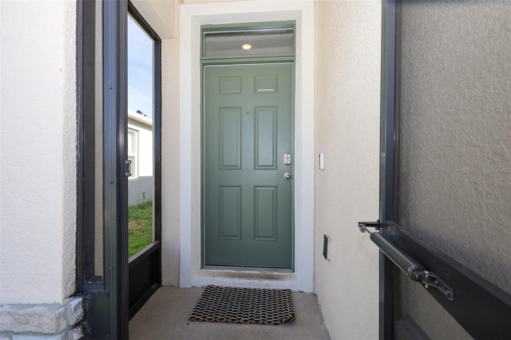 A sage green front door with a transom window sits within a screened-in entryway — 6310 CANTER CIRCLE, APOPKA, FL