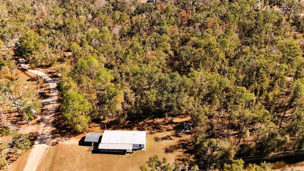 An aerial view shows a single-story house with a metal roof surrounded by dense woods — Lot 26 NW White Oak Way, FL 32053, FL