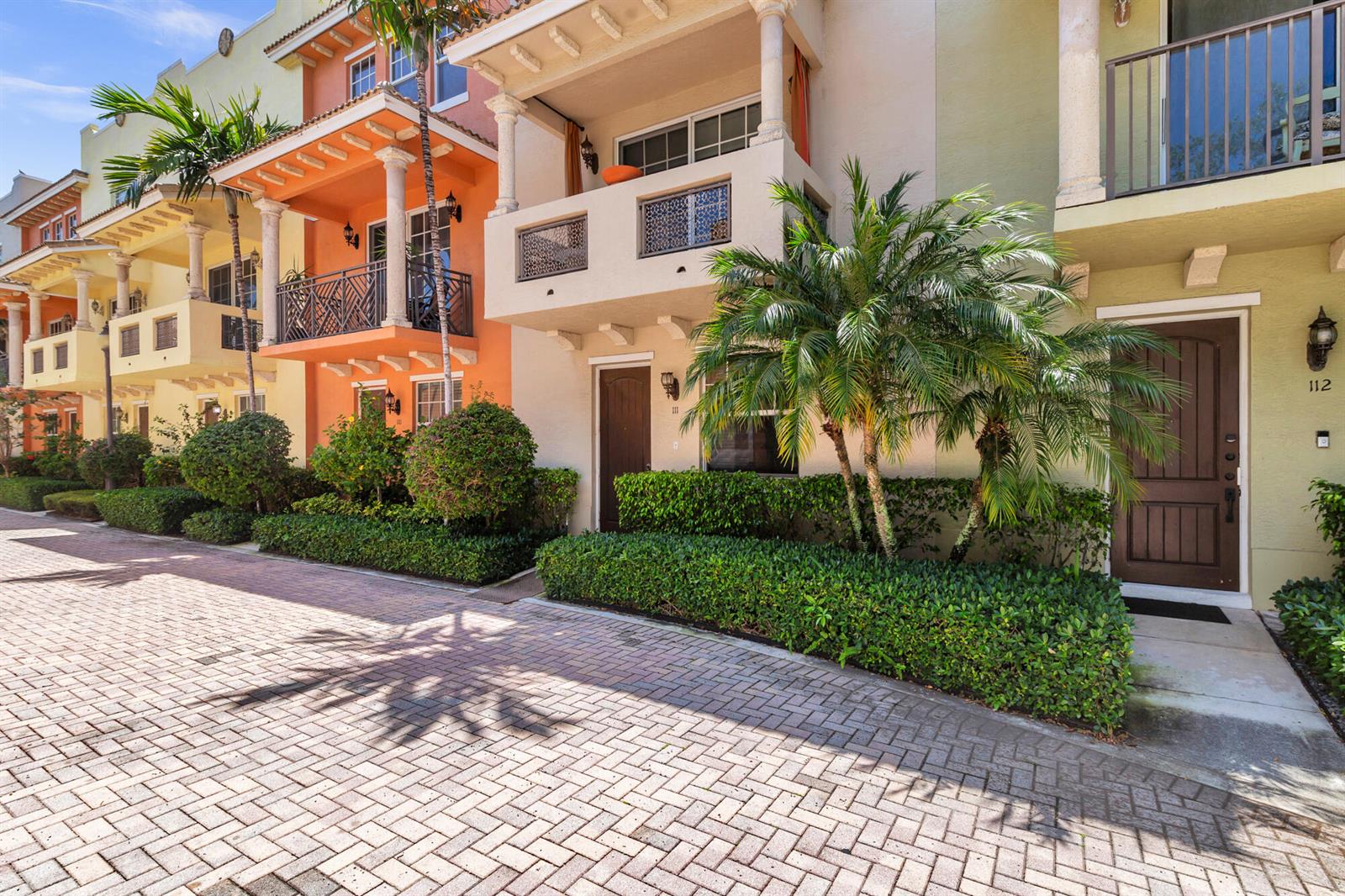 A row of colorful townhouses with balconies, palm trees, and a brick-paved street in front — 219 N L Street # 111, FL 33460, FL