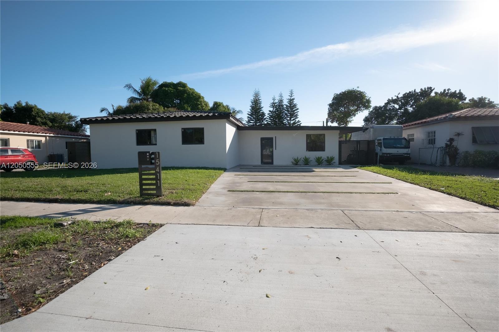 A single-story white house features a concrete driveway with grass strips and a modern mailbox — 15411 NE 10th Ave, North Miami Beach FL 33162, NORTH MIAMI BEACH, FL