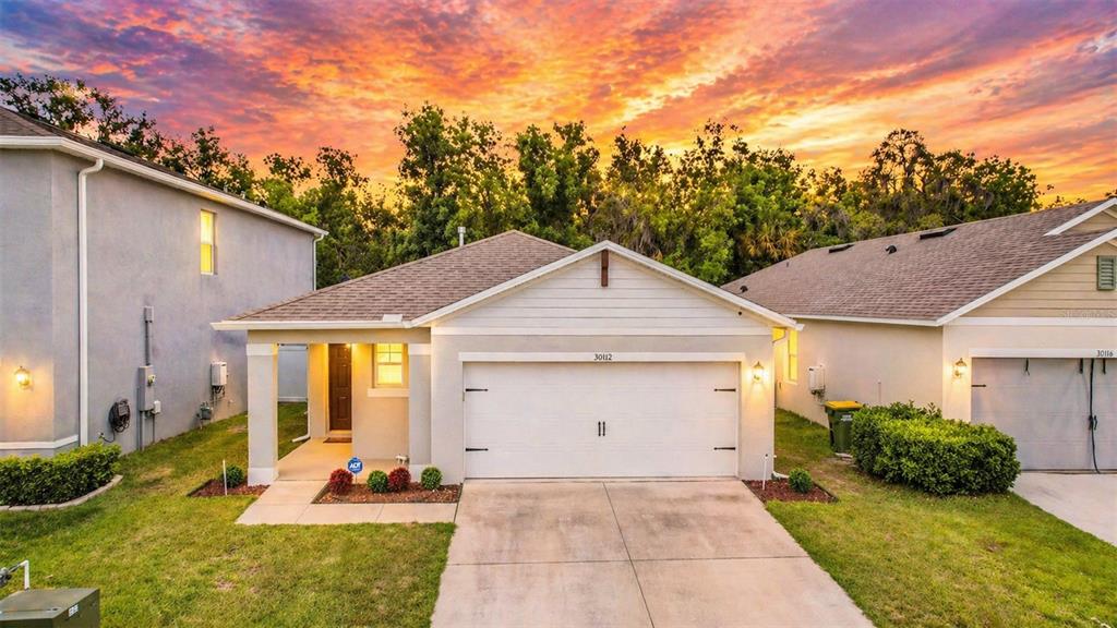 A single-story suburban house with a white garage and a covered entryway at sunset — 30112 ARMENIA ROAD, LEESBURG, FL