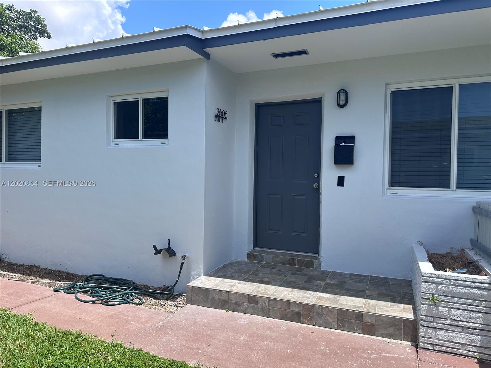 The exterior of a white house features a gray front door, tiled steps, and windows — 2806 SW 35th Ave # 1, Miami FL 33133, MIAMI, FL