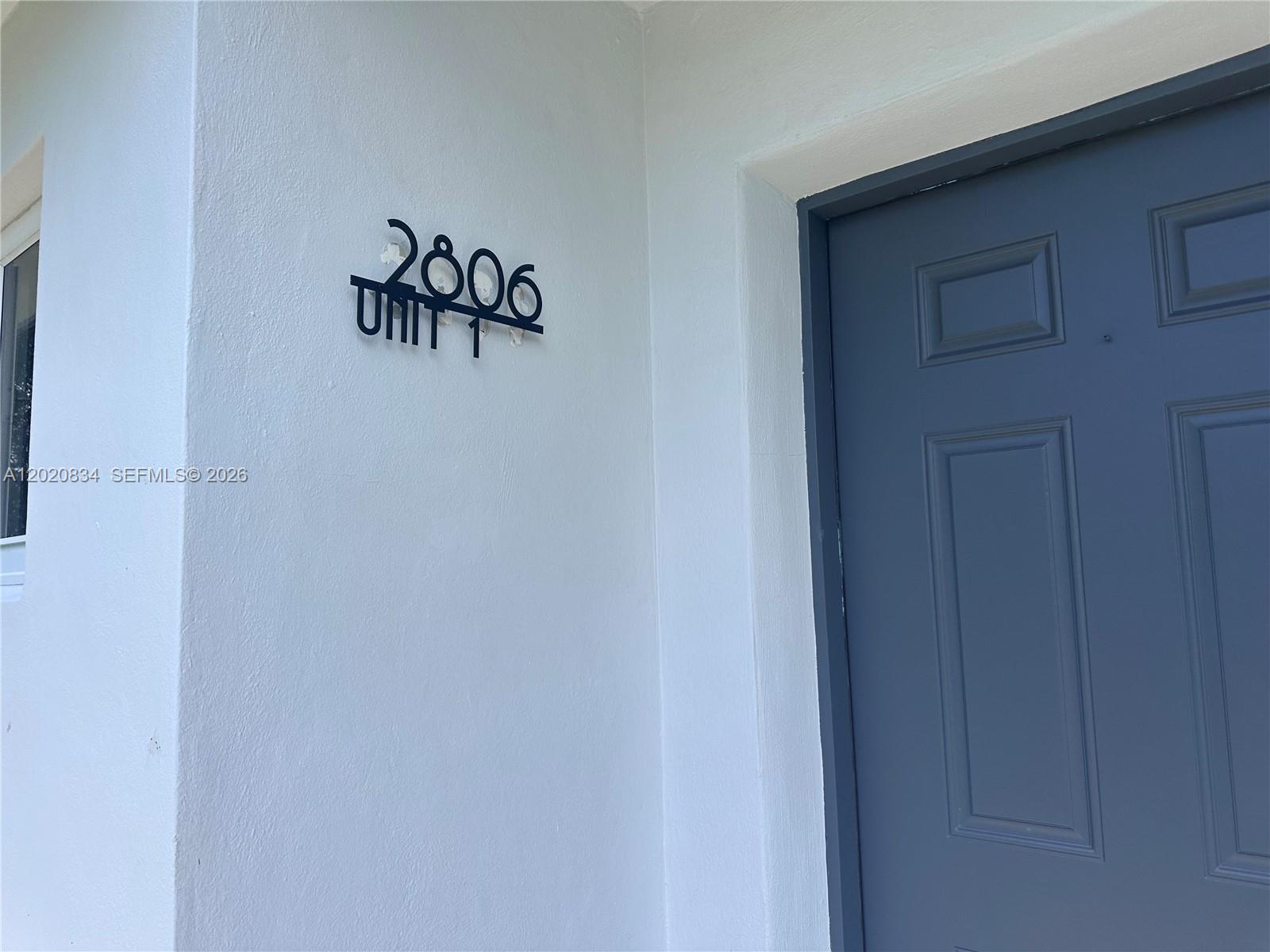 A blue door is set into a white exterior wall with a metal address sign — 2806 SW 35th Ave # 1, Miami FL 33133, MIAMI, FL