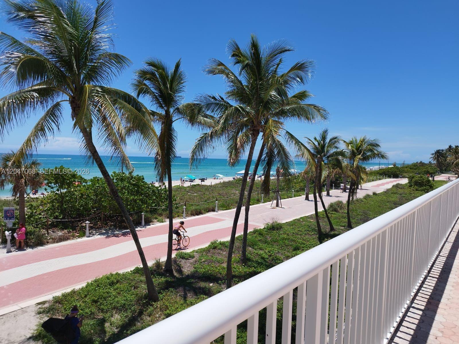 A balcony view overlooks a paved path, palm trees, and a beach with the ocean — 5401 Collins Ave # 1110, Miami Beach FL 33140, MIAMI BEACH, FL