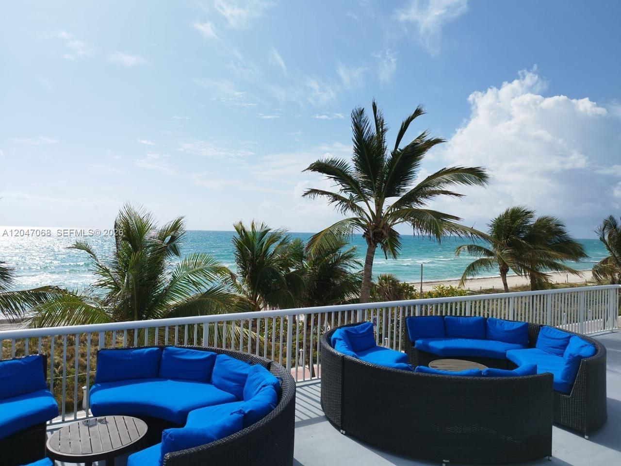A balcony features two curved wicker sofas with blue cushions overlooking the ocean and beach — 5401 Collins Ave # 1110, Miami Beach FL 33140, MIAMI BEACH, FL