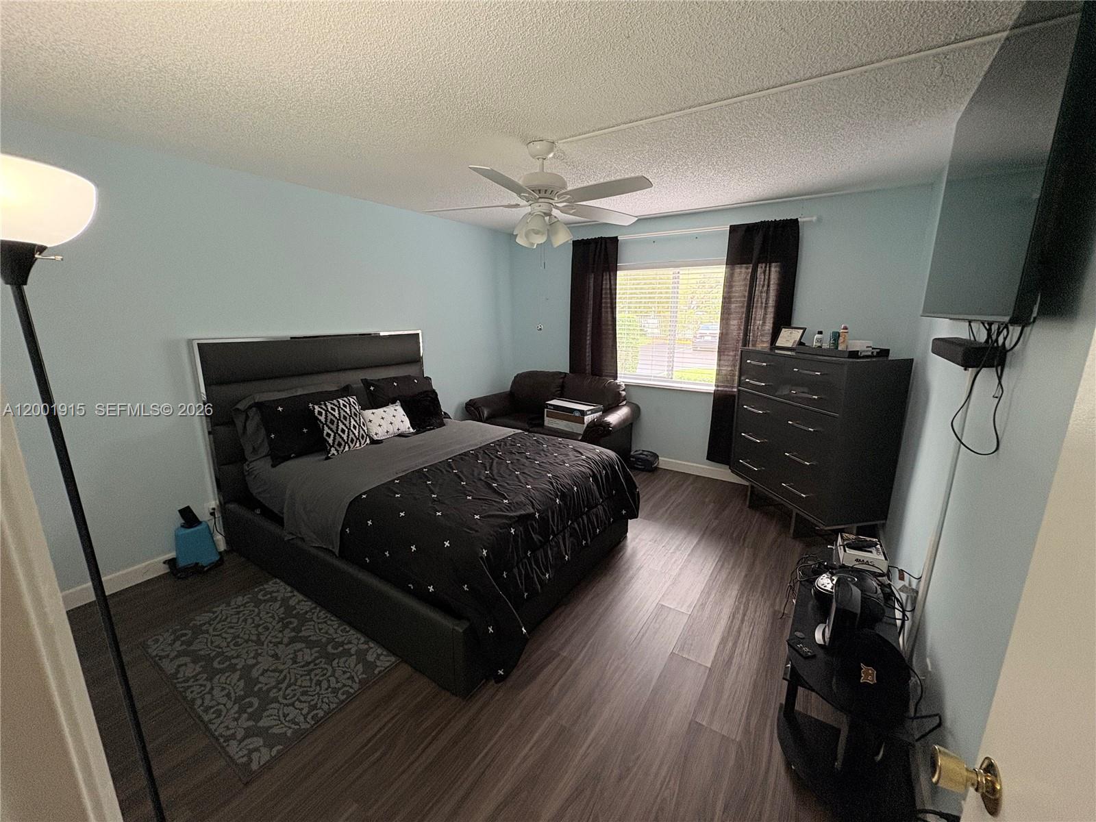 A bedroom features light blue walls, dark wood-look flooring, a black bed, and a dresser — 2769 S Oakland Forest Dr # 101, Oakland Park FL 33309, OAKLAND PARK, FL