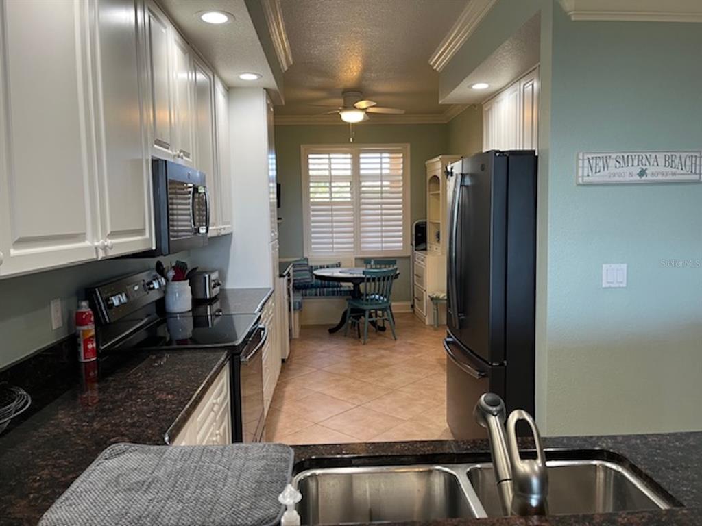A kitchen with white cabinets, dark countertops, a black refrigerator, and a breakfast nook area — 265 MINORCA BEACH WAY UNIT 304, NEW SMYRNA BEACH, FL