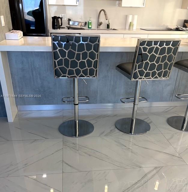 Two modern bar stools with geometric patterned backs sit at a kitchen island with marble floors — 19667 Turnberry Way # 27E, Aventura FL 33180, AVENTURA, FL