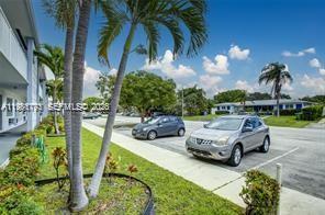 A parking lot with two cars sits beside a multi-story building and palm trees — 2020 NE 51st Ct # 203, Fort Lauderdale FL 33308, FORT LAUDERDALE, FL