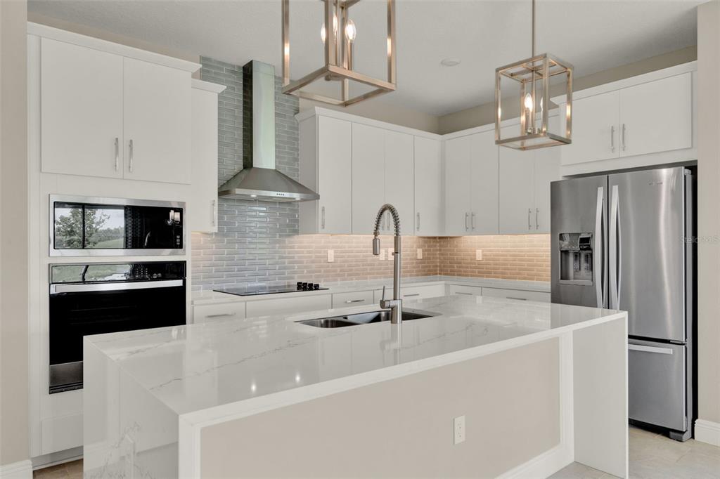 A modern kitchen features white cabinetry, a quartz island, stainless steel appliances, and subway tile — 2063 KEYSTONE PASS BOULEVARD, MINNEOLA, FL
