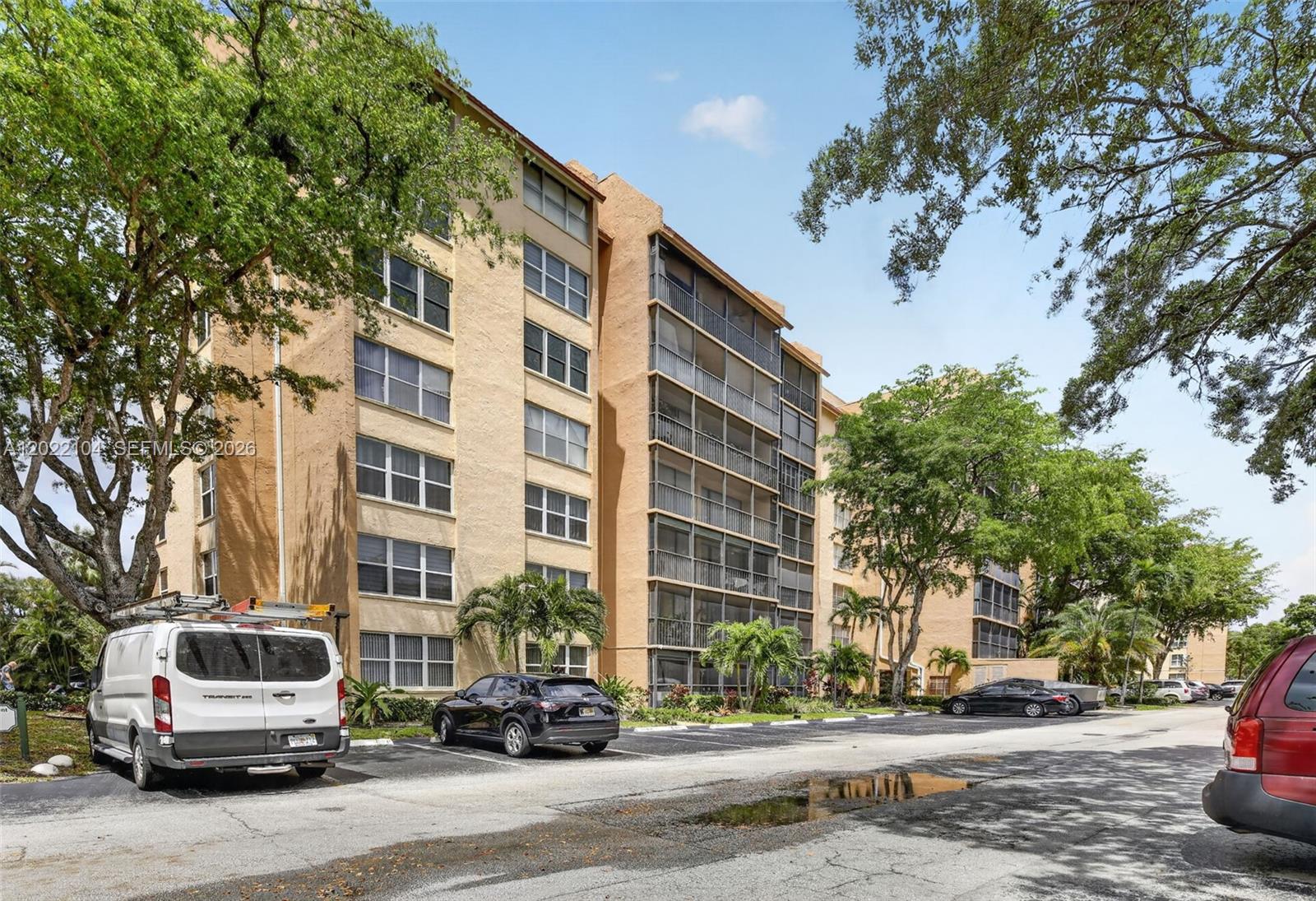A multi-story tan apartment building stands behind a parking lot with several parked vehicles — 3771 Environ Blvd # 355, Lauderhill FL 33319, LAUDERHILL, FL