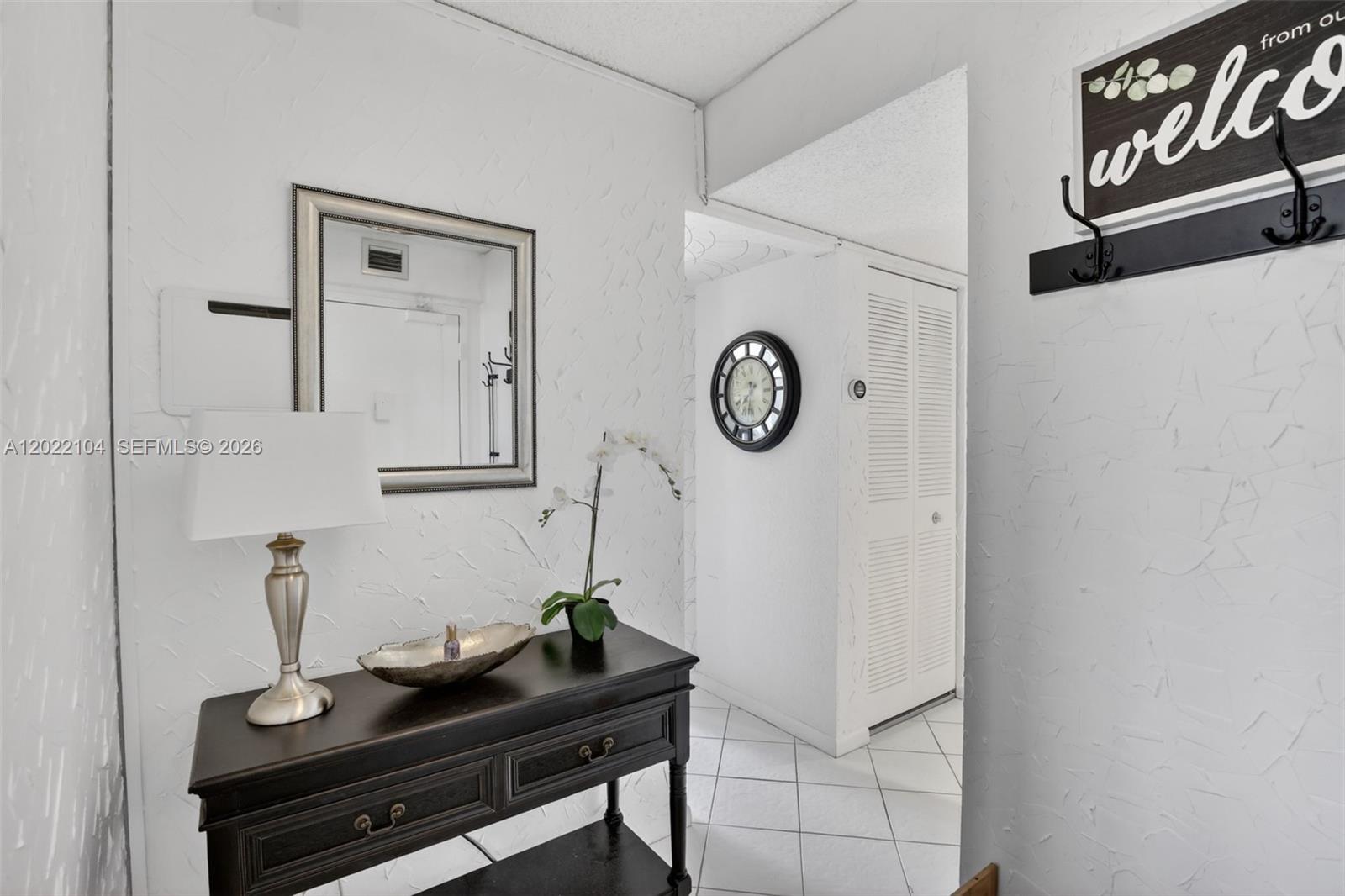 A white-walled entryway features a dark wood console table, a mirror, and a wall clock — 3771 Environ Blvd # 355, Lauderhill FL 33319, LAUDERHILL, FL