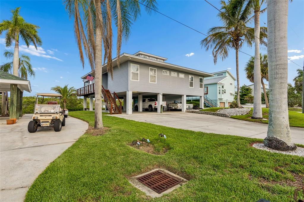 A stilt house with a concrete driveway, a golf cart, and palm trees under blue skies — 119 BURNS ROAD, TERRA CEIA, FL