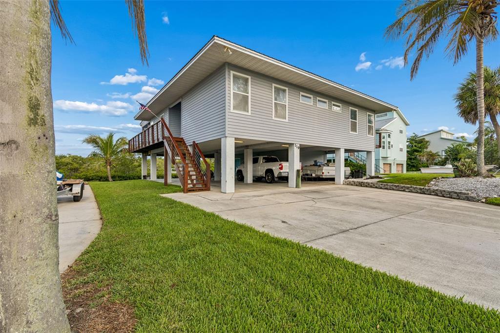 An elevated gray house with a concrete driveway and a wooden staircase sits outdoors — 119 BURNS ROAD, TERRA CEIA, FL