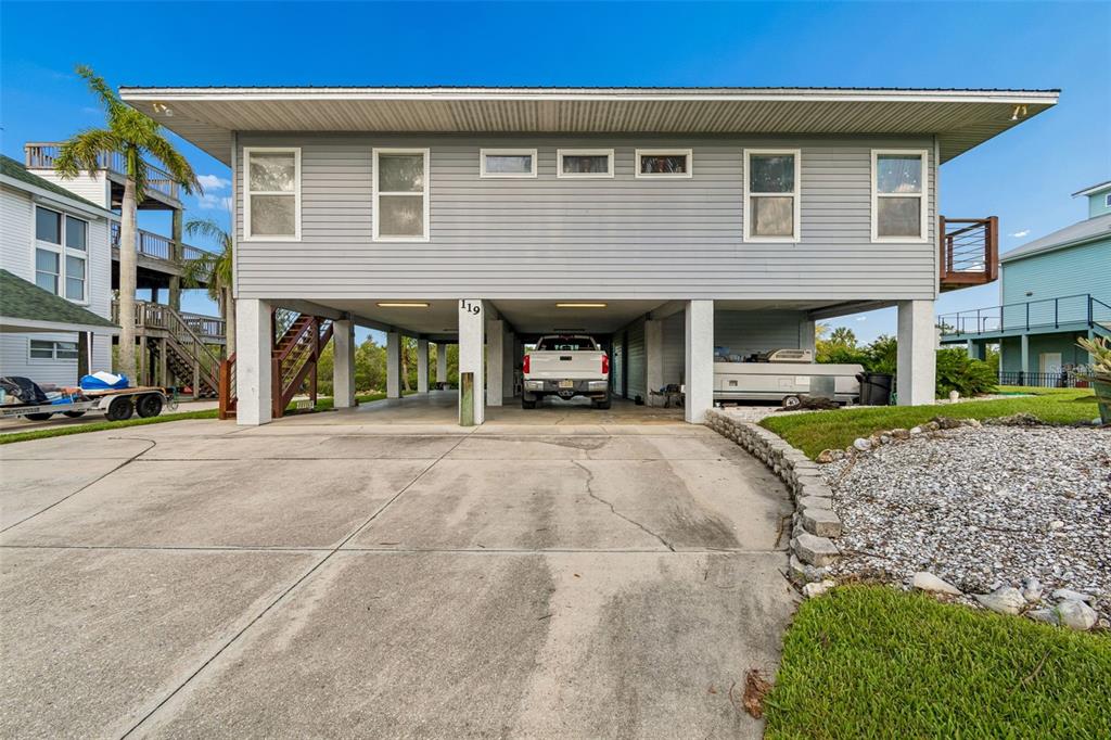 A stilt house with a concrete driveway, covered parking area, and gray horizontal siding — 119 BURNS ROAD, TERRA CEIA, FL