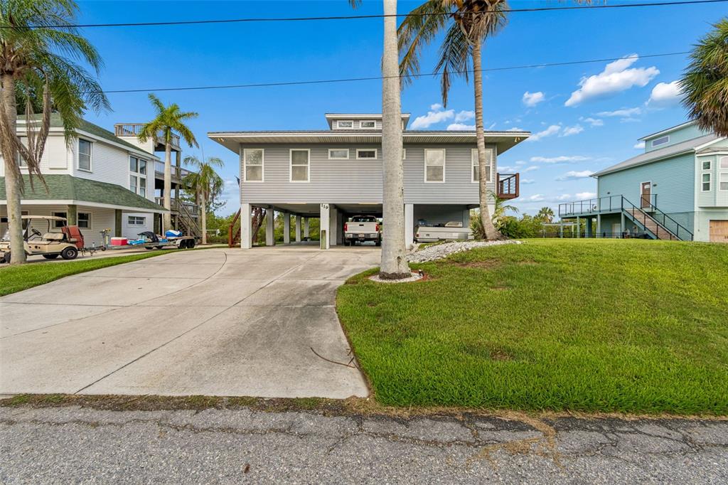 A gray stilt house with a concrete driveway and palm trees under a blue sky — 119 BURNS ROAD, TERRA CEIA, FL