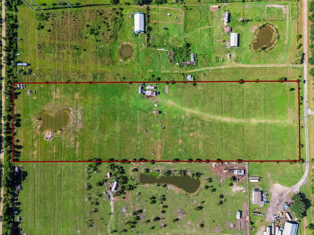 An aerial view shows a rectangular plot of land with a pond and small structures — 345 TROTTING TRAIL, OSTEEN, FL