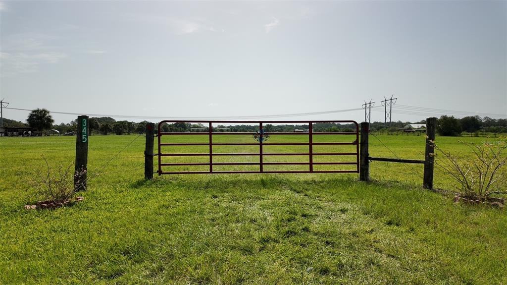 A red metal gate stands in a grassy field between two wooden fence posts — 345 TROTTING TRAIL, OSTEEN, FL