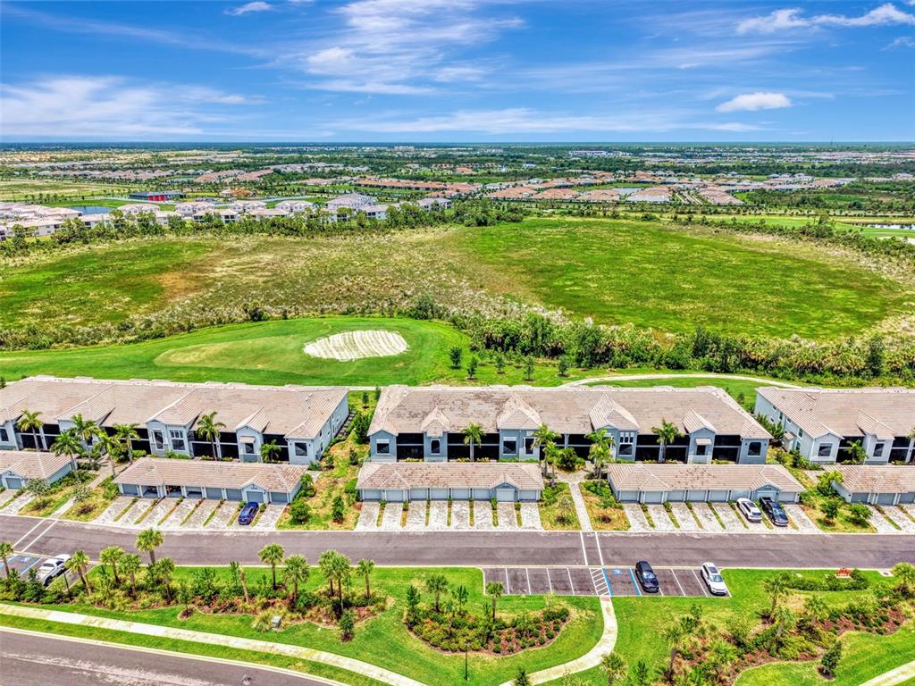 An aerial view shows a row of townhomes adjacent to a golf course and parking — 12520 GALAPAGOS COURT UNIT 102, VENICE, FL