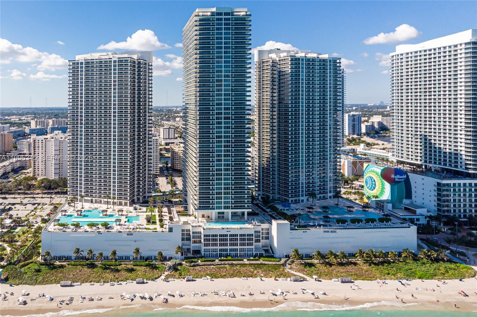 An aerial view shows three tall residential towers situated directly on a sandy beach — 1830 S Ocean Dr # 1501, Hallandale Beach FL 33009, HALLANDALE BEACH, FL