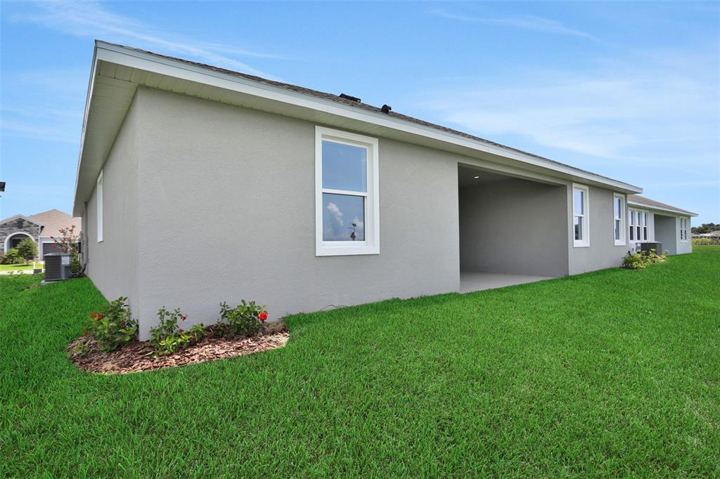 The exterior of a gray stucco house features a covered patio and a grassy yard — 7418 SEA MANATEE STREET, PARRISH, FL