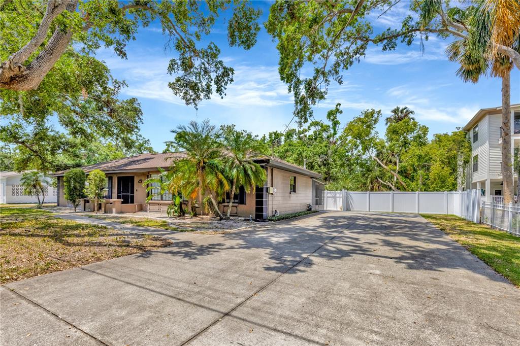 A single-story house with a large concrete driveway, palm trees, and a white privacy fence — 4909 S ELBERON STREET, TAMPA, FL