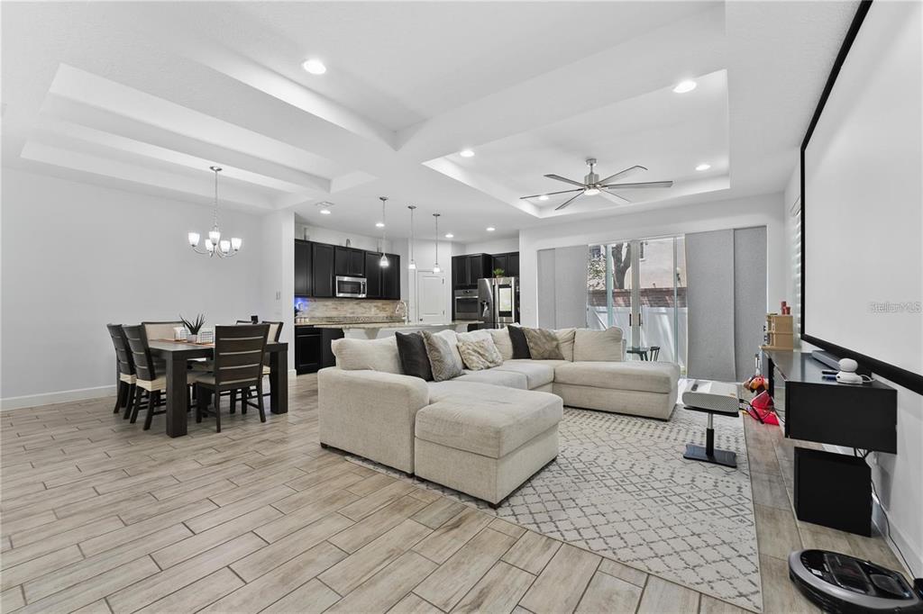 An open-concept living and dining area with a large sectional, tray ceilings, and tile flooring — 572 LAKE WILDMERE COVE, LONGWOOD, FL